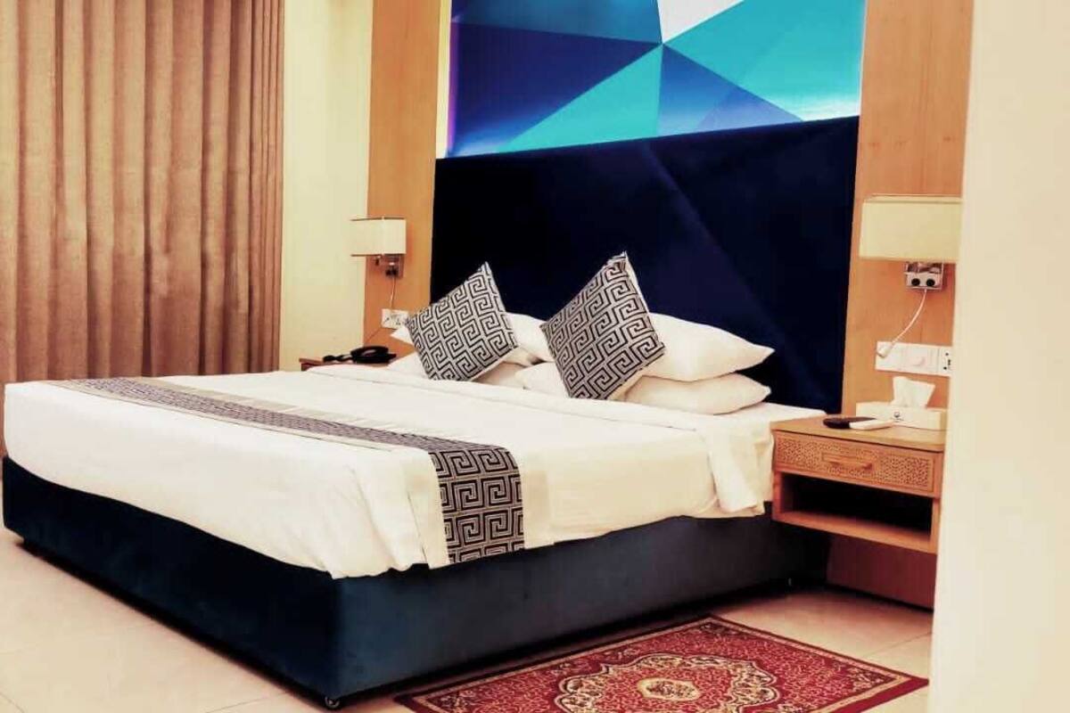 A hotel room with a bed, a blue armchair, a nightstand, and a wall-mounted TV.