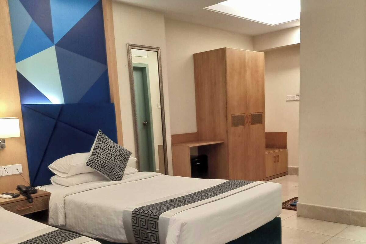 A hotel room with two beds, a wardrobe, a mirror, and a geometric wall design.