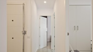 Un couloir avec une porte blanche sur la gauche, une armoire blanche sur la droite et un petit tabouret au centre.