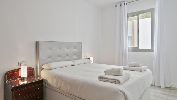 Une chambre à coucher moderne avec un grand lit, une table de chevet avec une lampe et une fenêtre avec des rideaux.