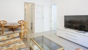 Un salon moderne comprenant un canapé, une table basse en verre, un téléviseur posé sur un meuble blanc, et un coin repas avec des chaises et une table.