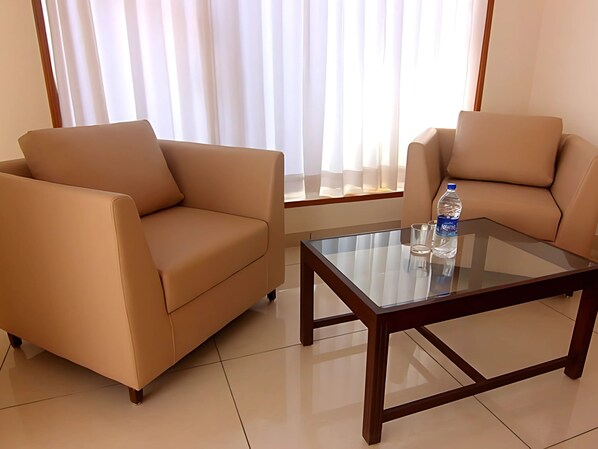 A modern living room with two beige sofas and a glass coffee table. - SRIJAN INN (Abu Road)