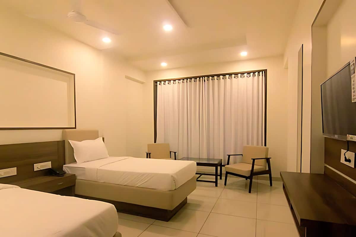 A hotel room with two beds, a desk, chairs, a TV, and a window with curtains.