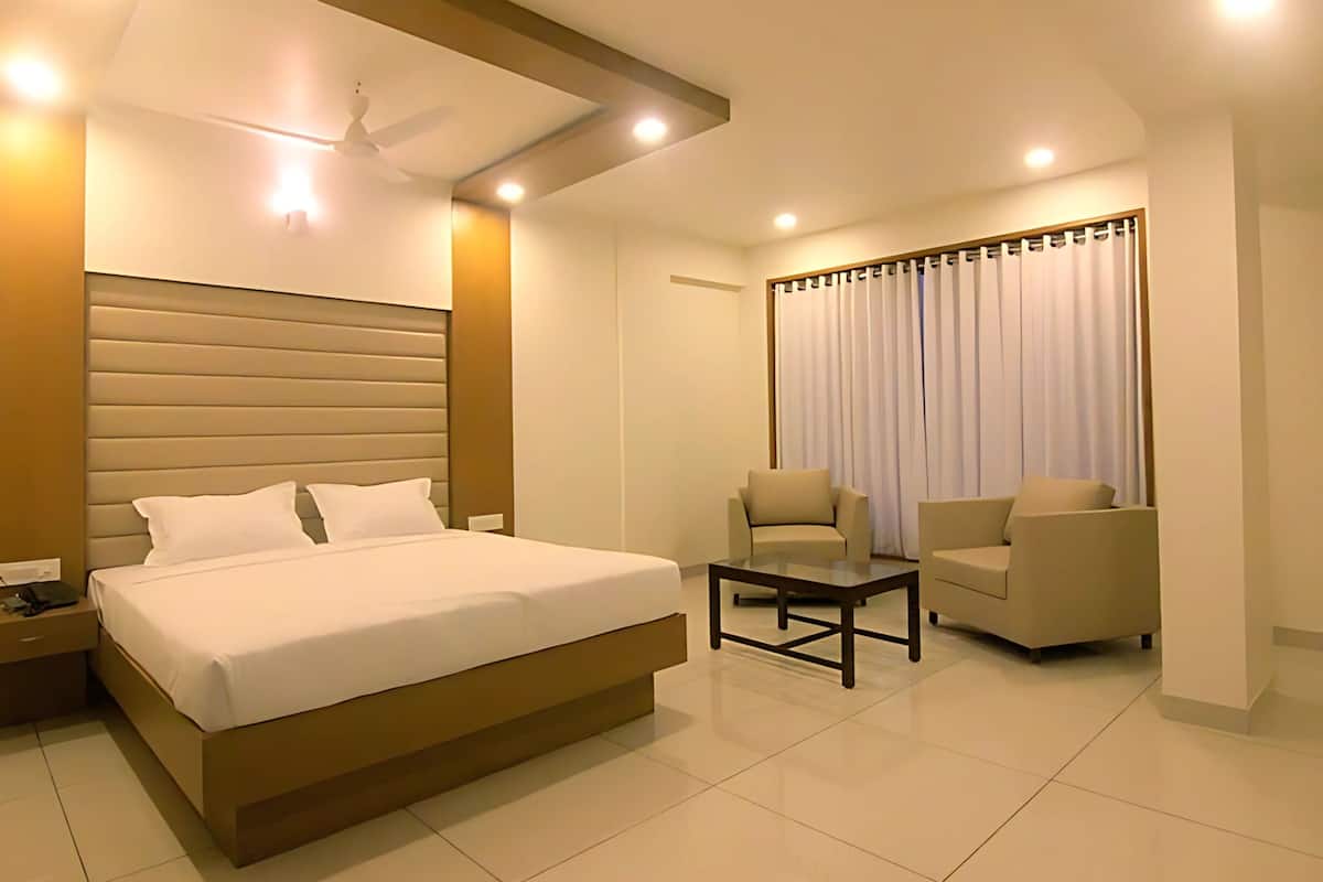 A modern hotel room with a large bed, a desk, two chairs, and a ceiling fan.