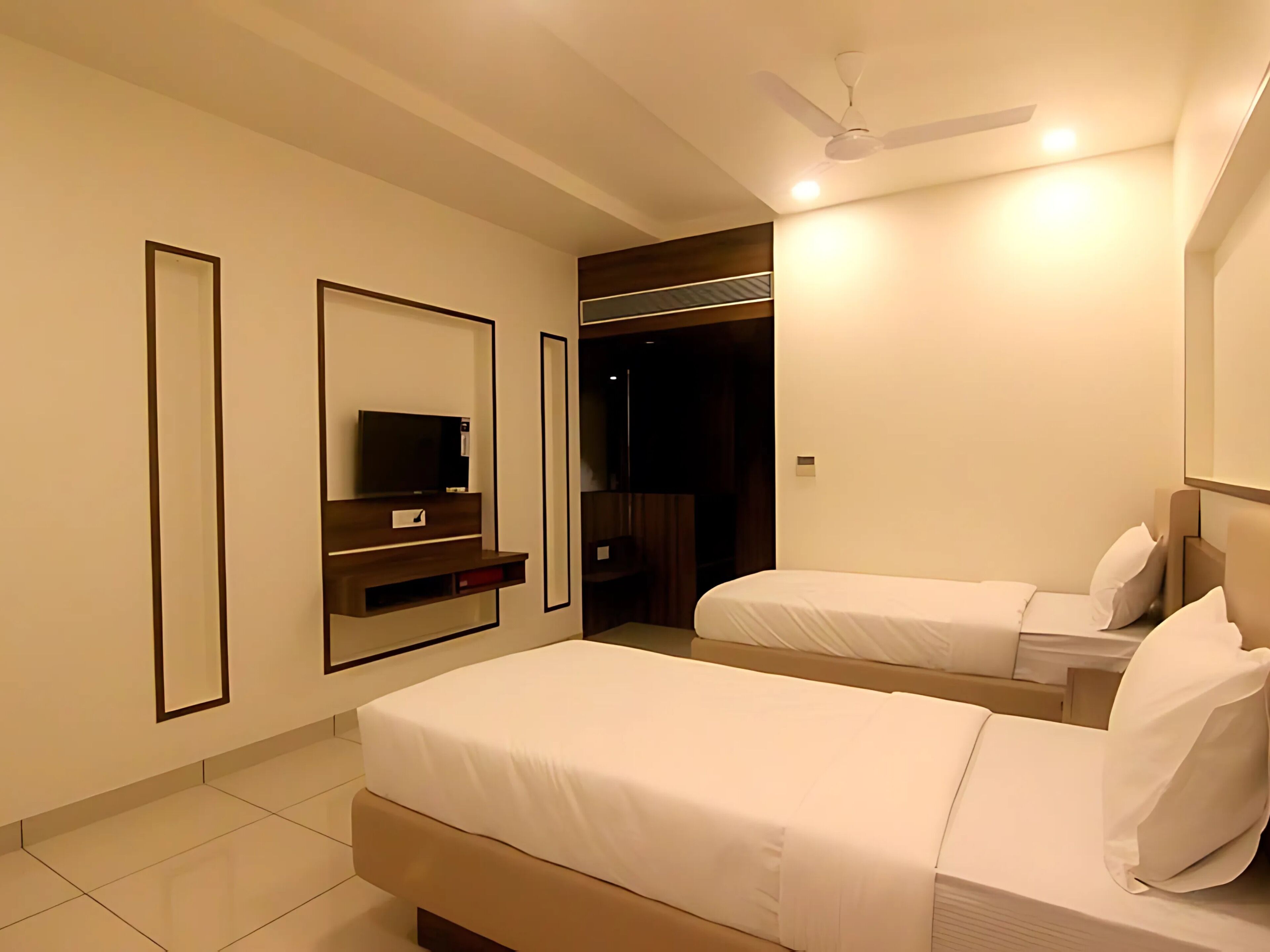 A hotel room with two beds, a TV, a wardrobe, and a ceiling fan.