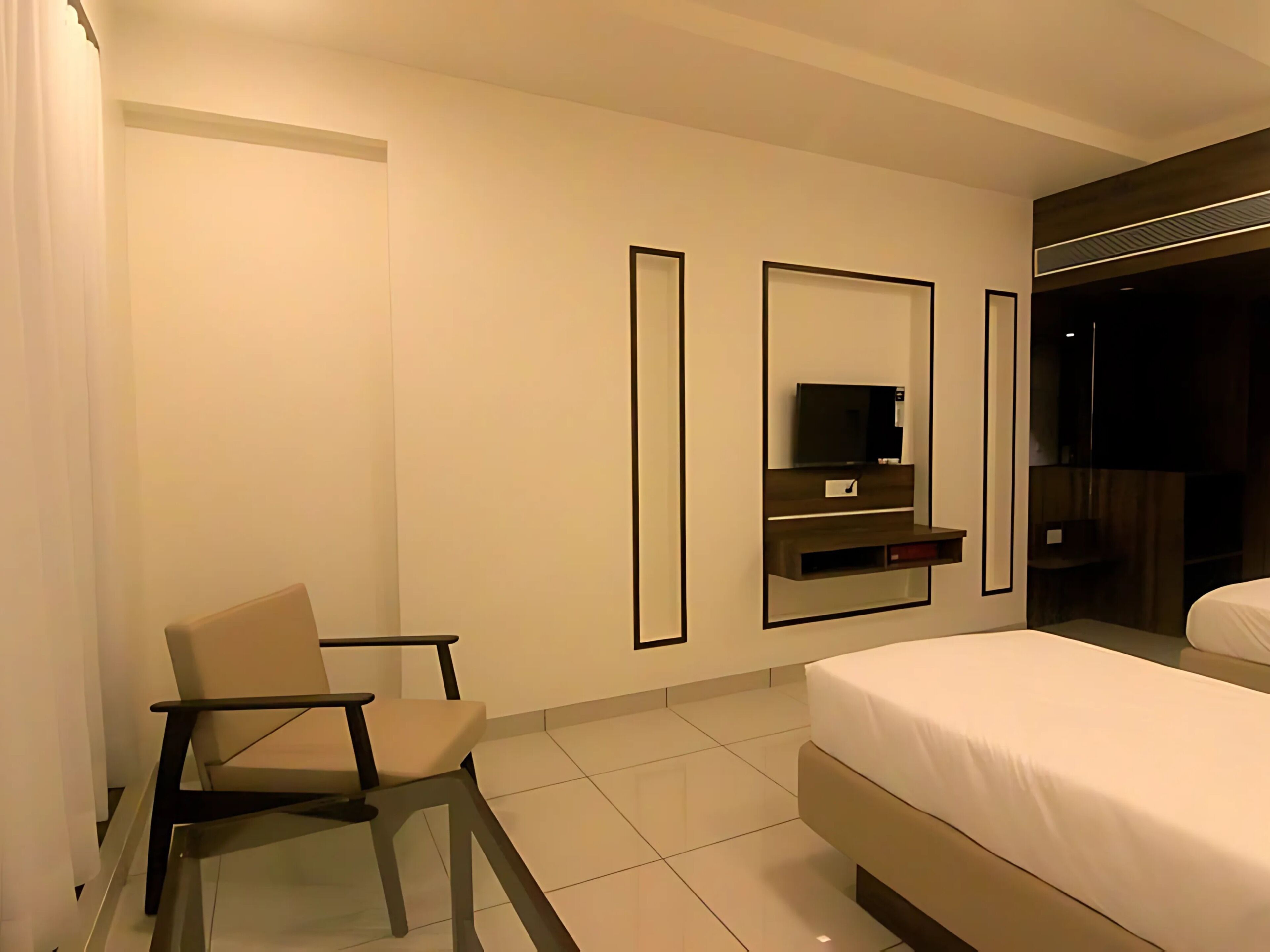 Una camera d'albergo moderna con un letto, una sedia, una televisione e uno specchio.