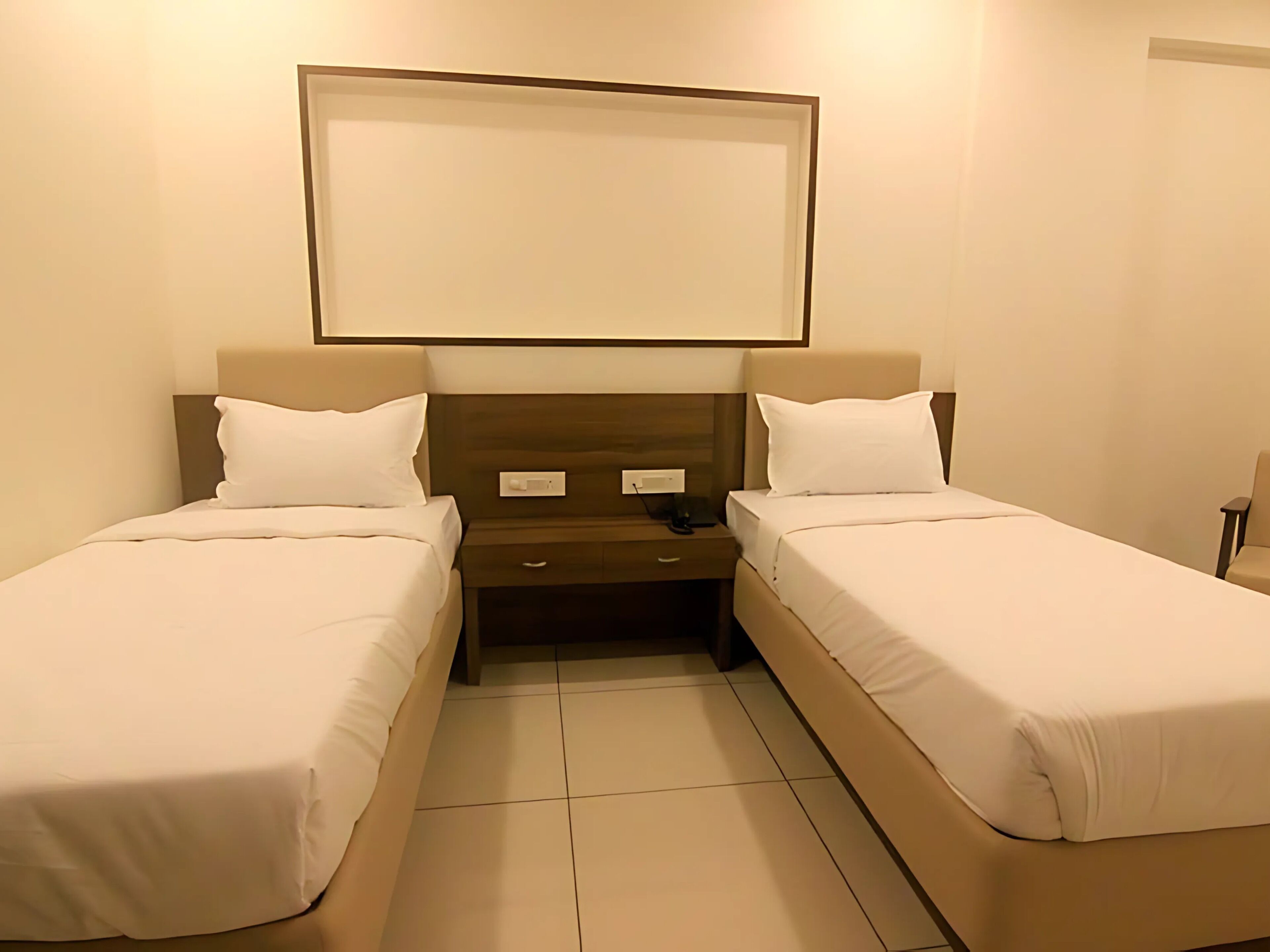 Una habitación de hotel con dos camas individuales, una mesita de noche y una lámpara de pared.