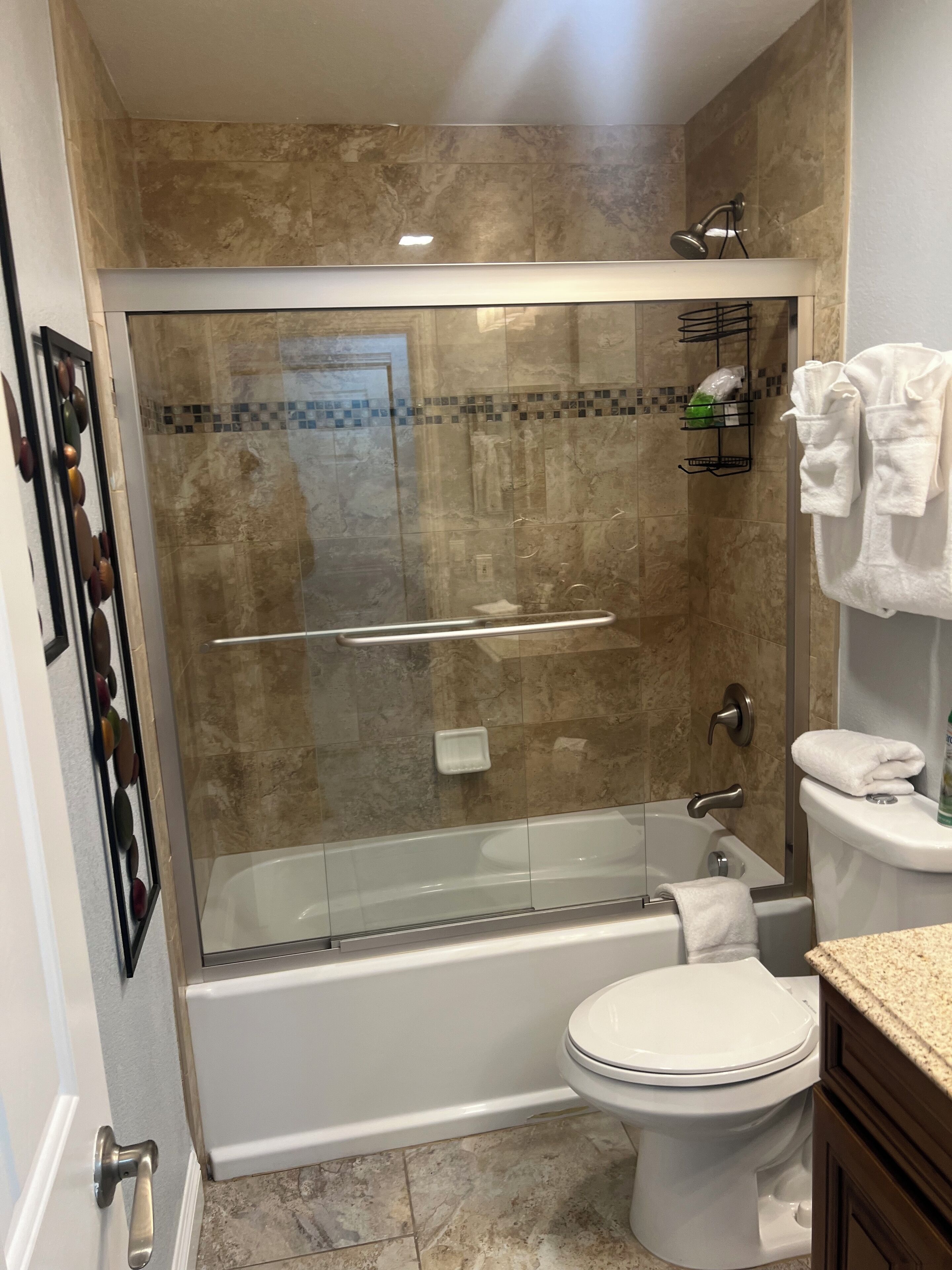Et moderne badeværelse med en bruseniche med glasvægge, et hvidt badekar og et toilet.