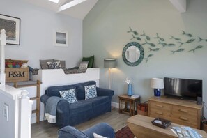A cozy living room with a blue sofa, a wooden coffee table, a TV, and a wall art of fish. - Beautiful Cottage on the Water Front, Polruan (Polruan)