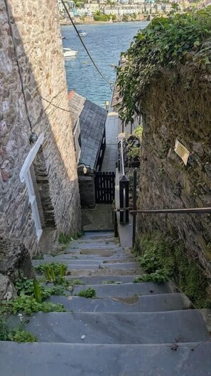 A narrow stone staircase leading down to a waterfront area with a view of the sea and buildings in the background.