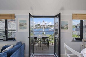 Ein Balkon mit Blick auf einen Hafen, mit Tisch und Stühlen, gerahmten Bildern an den Wänden und einem Blick auf die Stadt in der Ferne.