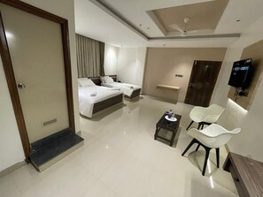 A hotel room with a bed, two chairs, a small table, a TV, and a bathroom.