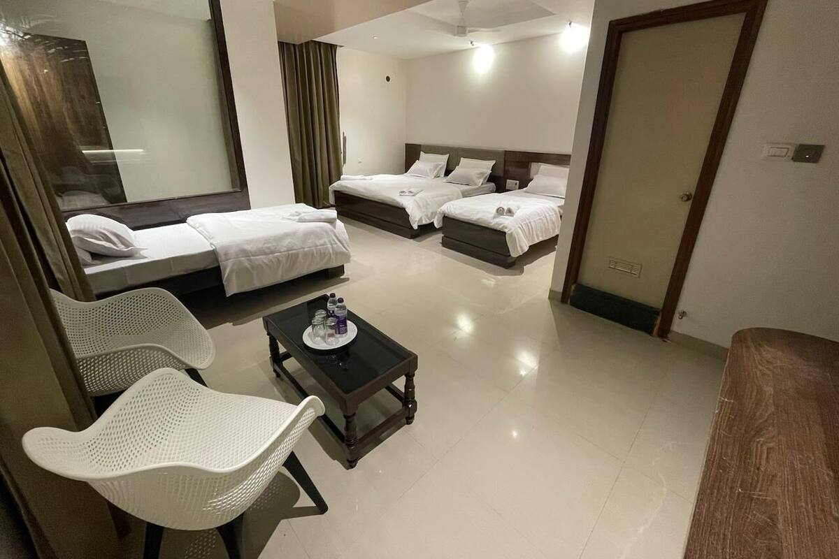 Une chambre d’hôtel avec deux lits, un coin salon avec une table et des chaises, un grand miroir et une porte.