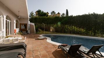A swimming pool with lounge chairs, a patio area, and a view of a forested hill.