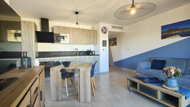 A modern kitchen with wooden cabinets, a built-in microwave, and a dining area with a table and chairs. - SAINT-AYGULF Sea view, 4 pers air conditioning, swimming pool, near Calanques corailleurs  (Fréjus)