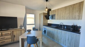 A modern kitchen with wooden cabinets, a microwave, and a sink. There is a dining table with chairs and a TV on the left. - SAINT-AYGULF Sea view, 4 pers air conditioning, swimming pool, near Calanques corailleurs  (Fréjus)