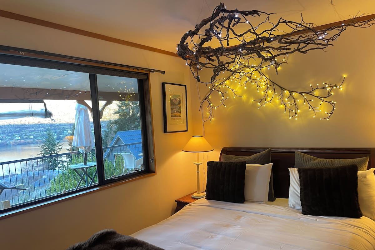 A bedroom with a large bed, a window with a view of a balcony, and a wall-mounted light fixture.