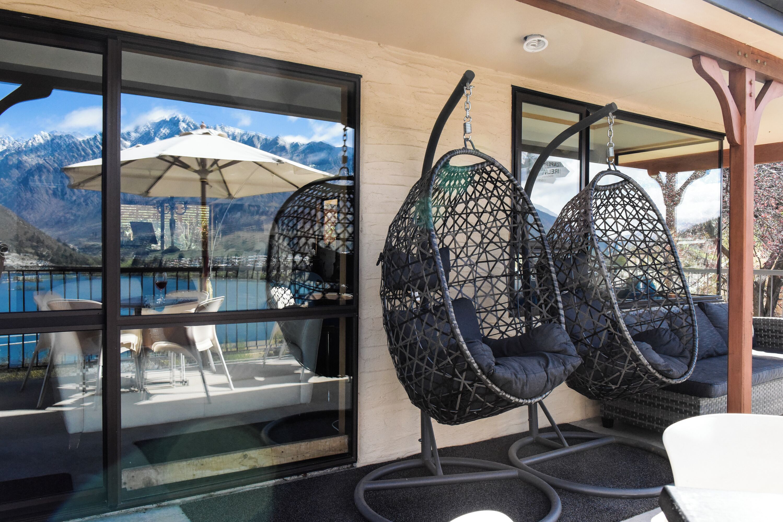 A terrace with hanging chairs, a table with chairs, and a view of mountains through large windows.
