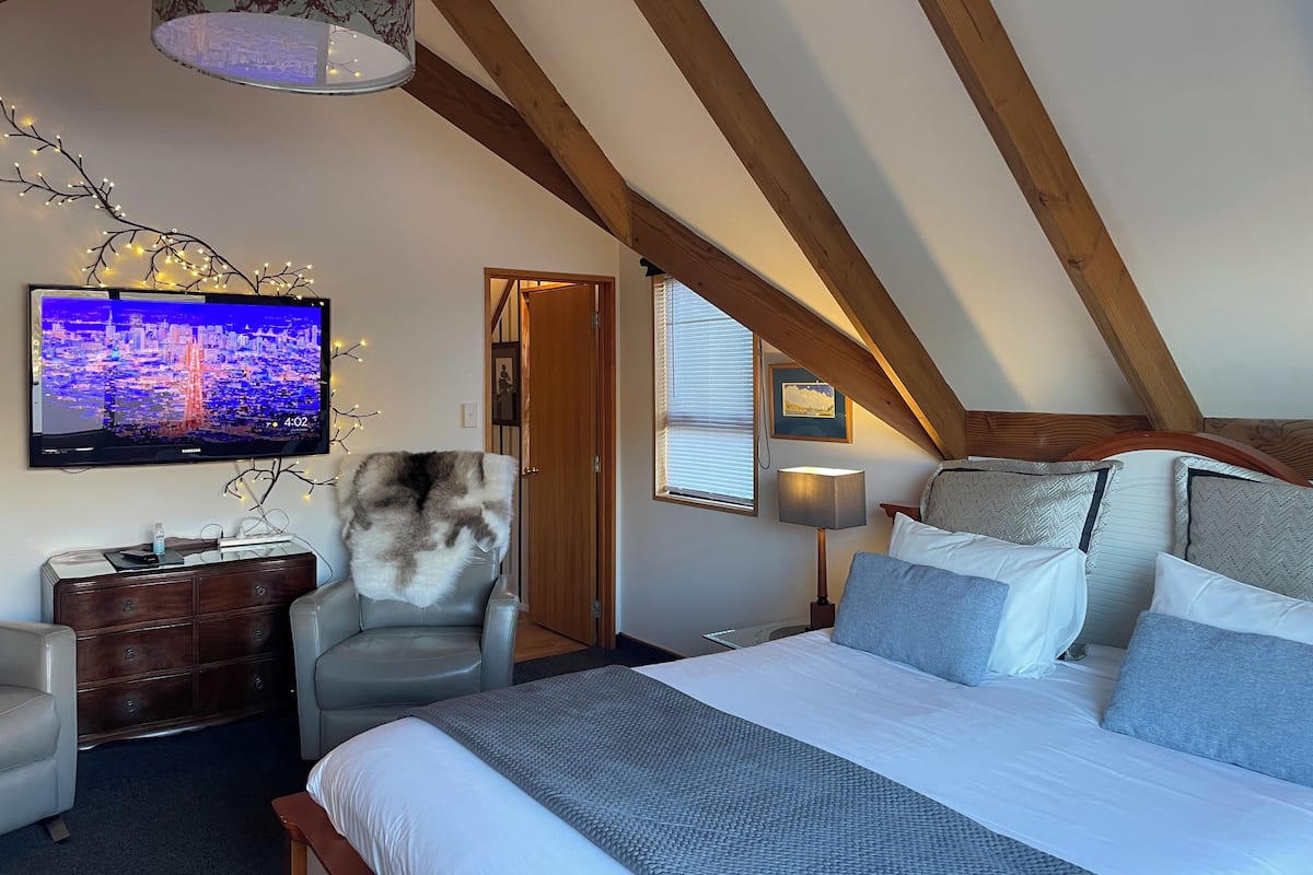 A bedroom with a bed, a chair, a TV, and a wooden ceiling.