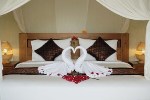 A bed with a canopy, two pillows, a bedside lamp, and a decorative arrangement of towels and flowers.