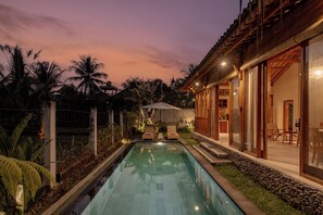 A swimming pool with a wooden deck, a covered seating area, and a view of the surrounding landscape.