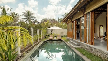 Una piscina con una vista despejada del cielo, rodeada de exuberante vegetación y una estructura de madera con grandes ventanales.
