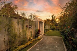 A pathway leading to a building with a stone facade, surrounded by bamboo and tropical plants.
