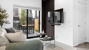 Un salon moderne comprenant un canapé, une table basse, un téléviseur fixé au mur et une porte-fenêtre coulissante donnant sur une terrasse extérieure.