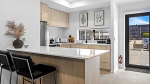 Une cuisine moderne dotée d’un îlot central, de meubles en bois et offrant une vue sur une concessionnaire Lexus à travers la porte vitrée.