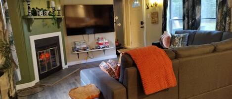 A living room with a sectional sofa, a flat-screen TV, a fireplace, and a wooden coffee table.