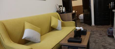 A yellow sofa with white cushions, a wooden coffee table, and a painting on the wall.