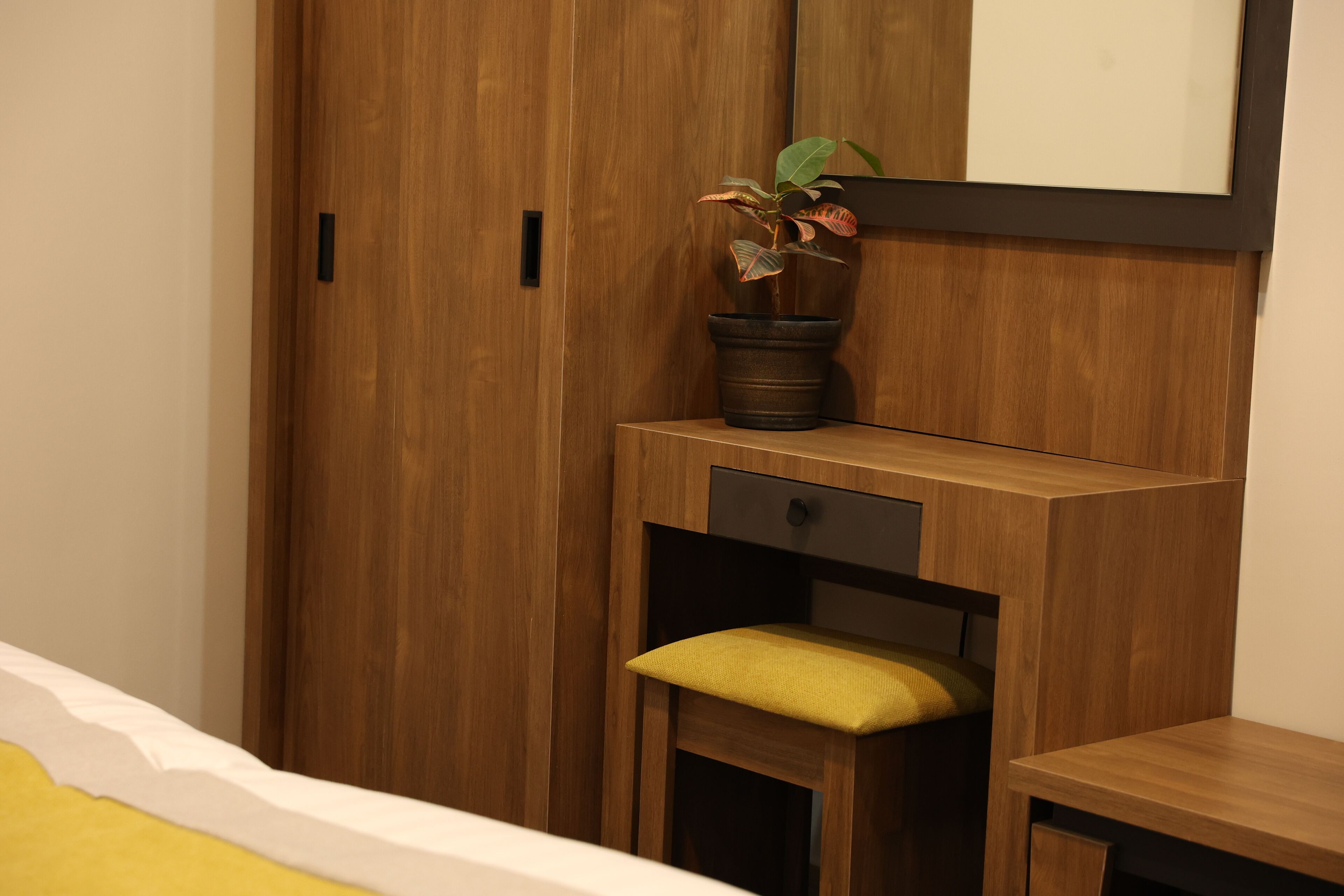 Une armoire en bois sur laquelle est posée une plante, un petit banc avec un coussin et un miroir accroché au mur.