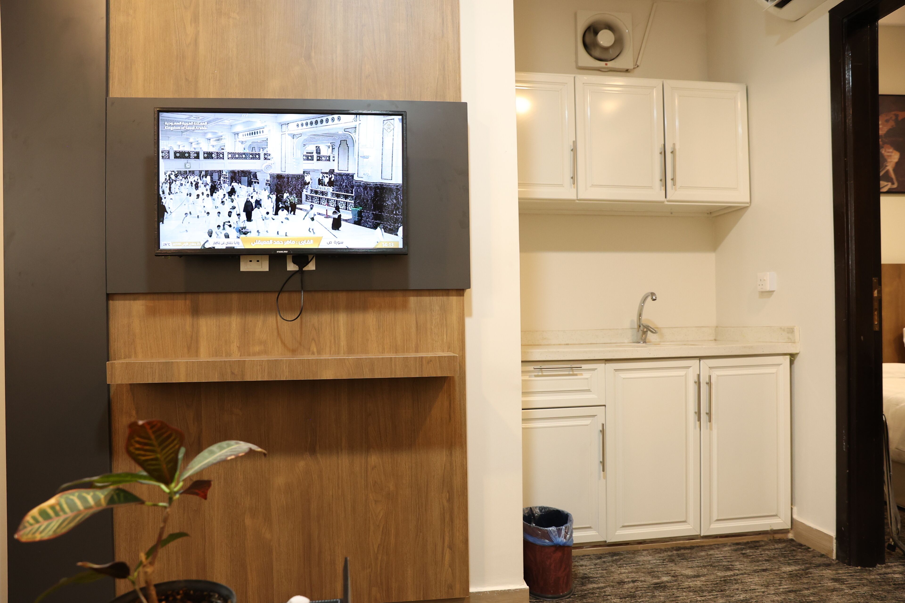 A television mounted on a wooden wall displaying a crowded indoor scene.