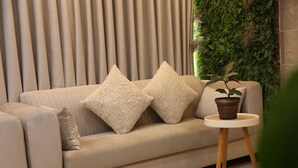 A beige sofa with patterned cushions, a small round table with a potted plant, and a green vertical garden behind it. - MADINAH ARAM HOTEL (Madinah)