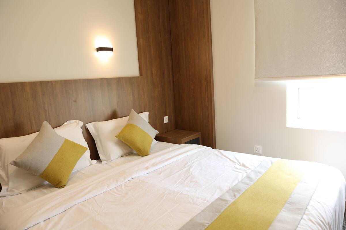 A neatly made bed with white bedding and two pillows, one with a yellow accent.