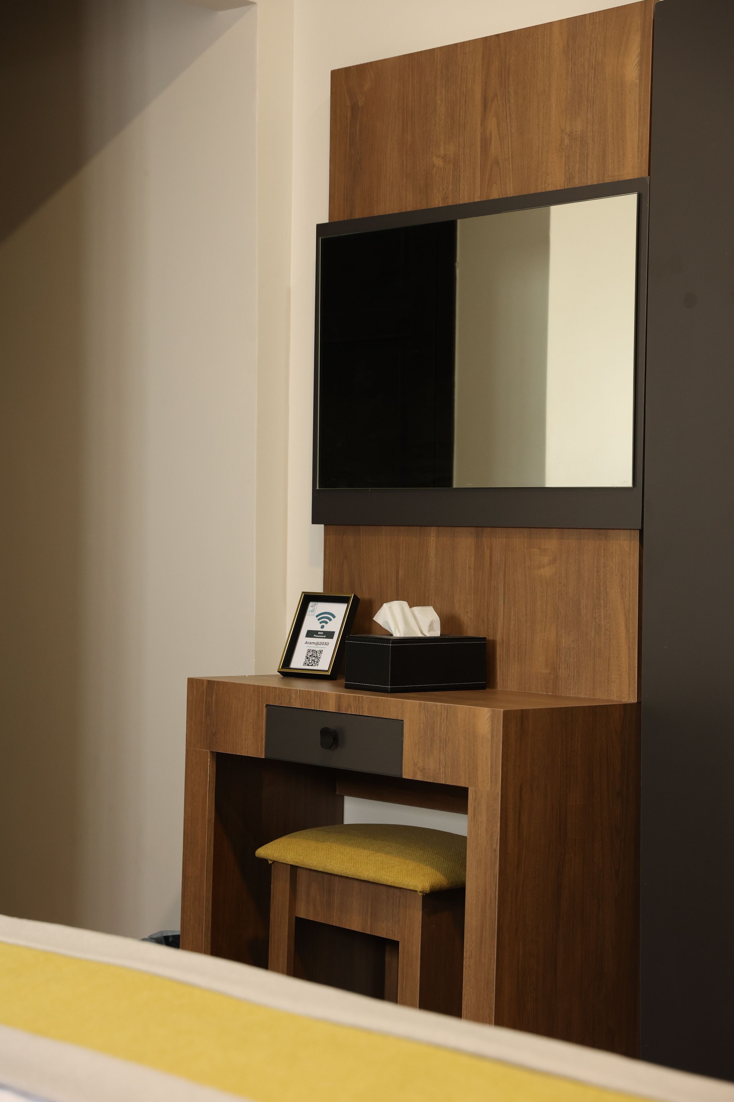 A wooden vanity with a mirror, a framed QR code, and a tissue box.