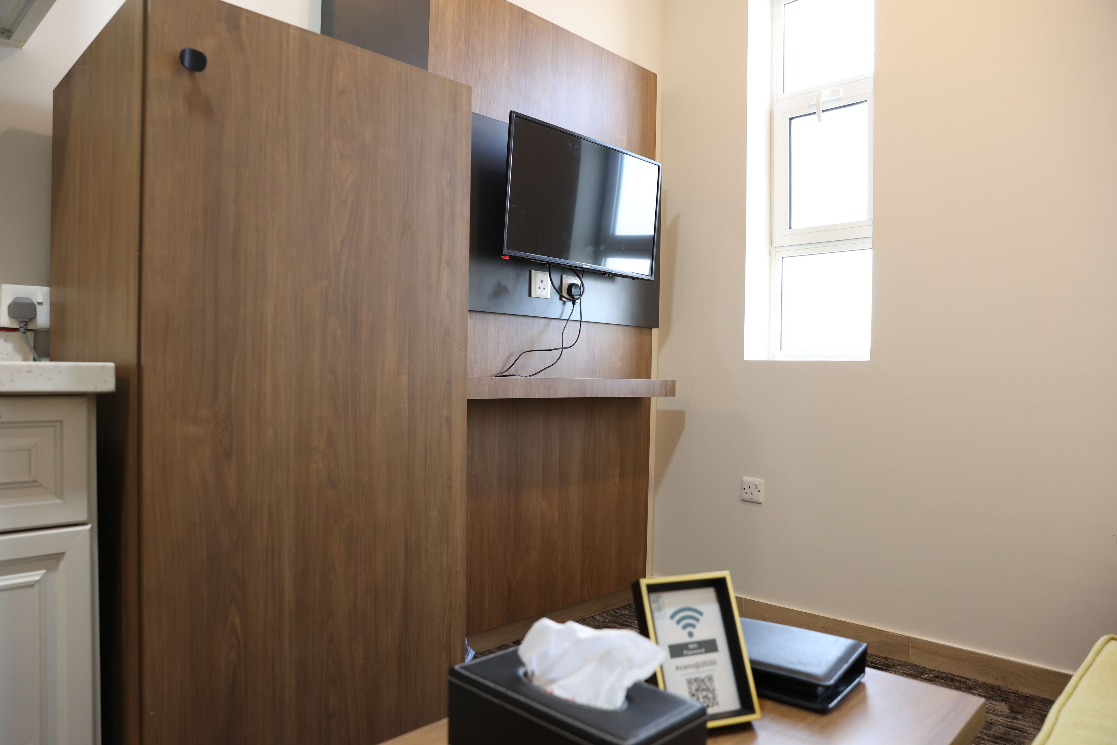 A room with a mounted TV, a wooden cabinet, a small table with a tissue box, and a framed picture.
