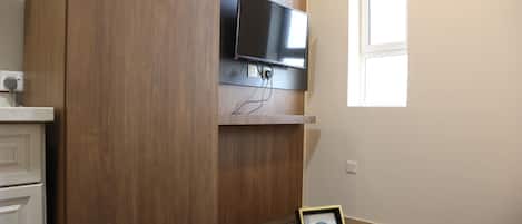 A room with a mounted TV, a wooden cabinet, a small table with a tissue box, and a framed picture.