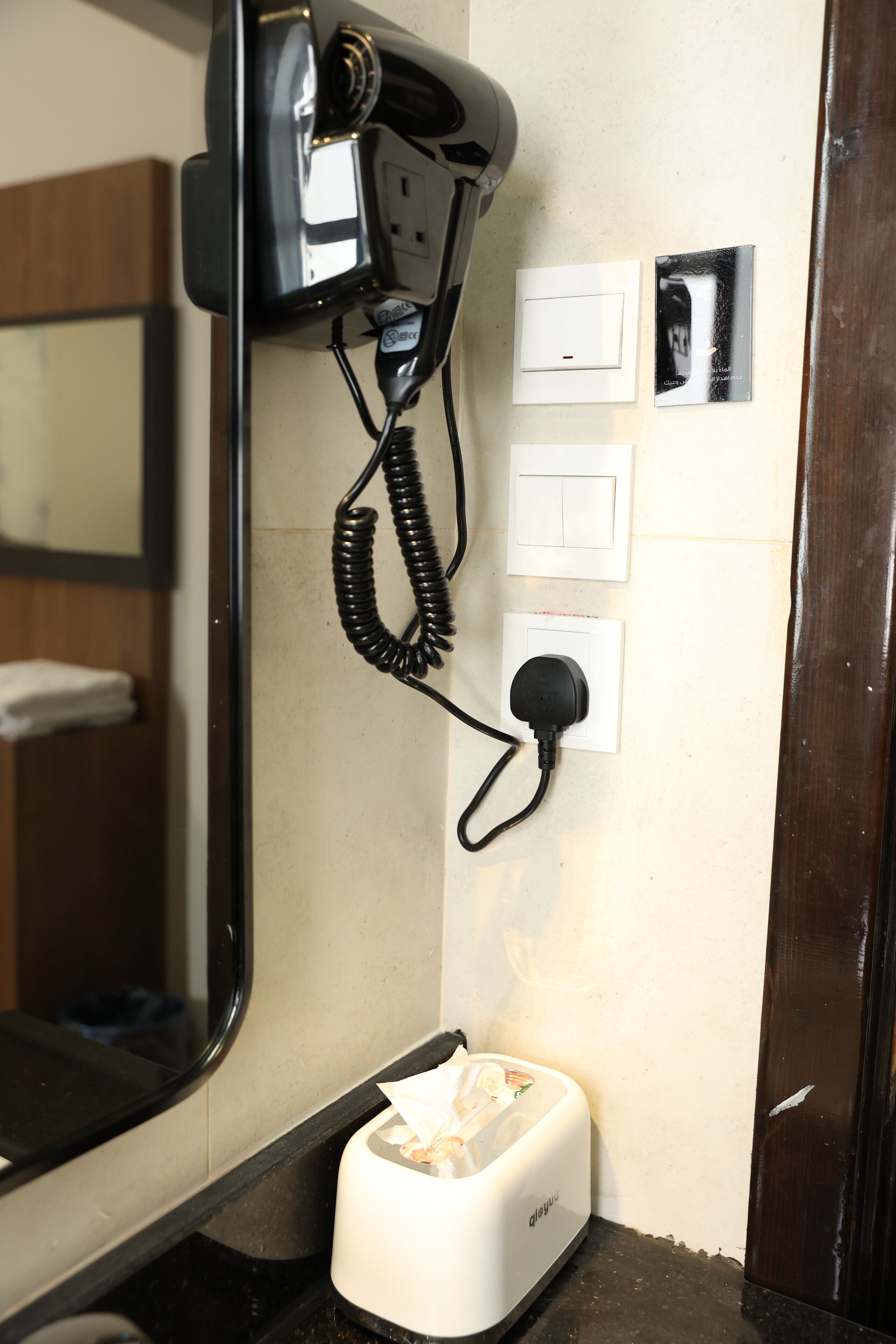 A hotel room with a hairdryer, a telephone, a tissue dispenser, and a mirror.