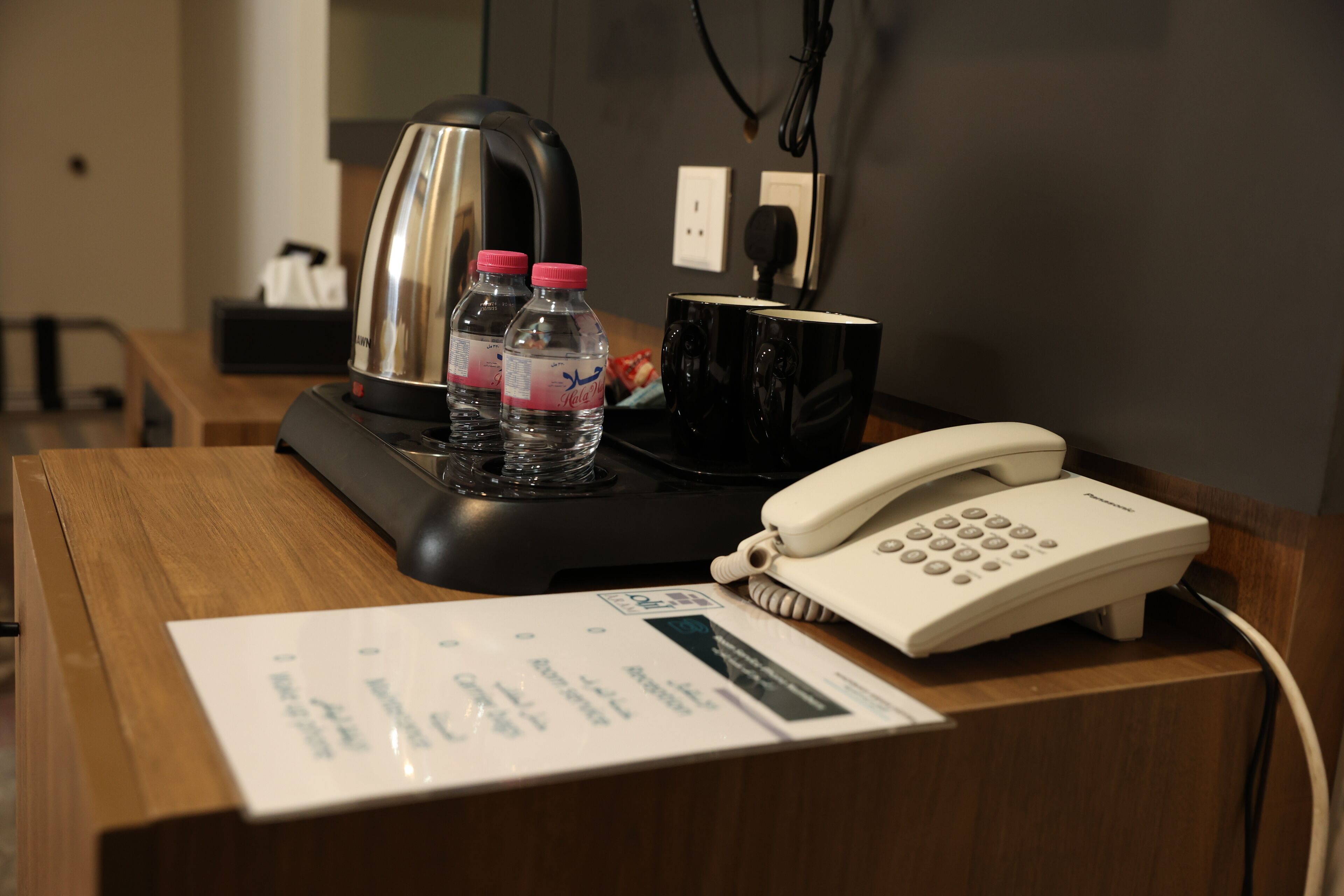 Ein Hotelrezeptionstresen mit Telefon, Kaffeemaschine, zwei Wasserflaschen und einer schwarzen Tasse.