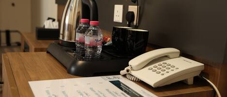 A hotel reception desk with a telephone, a coffee maker, two water bottles, and a black mug.