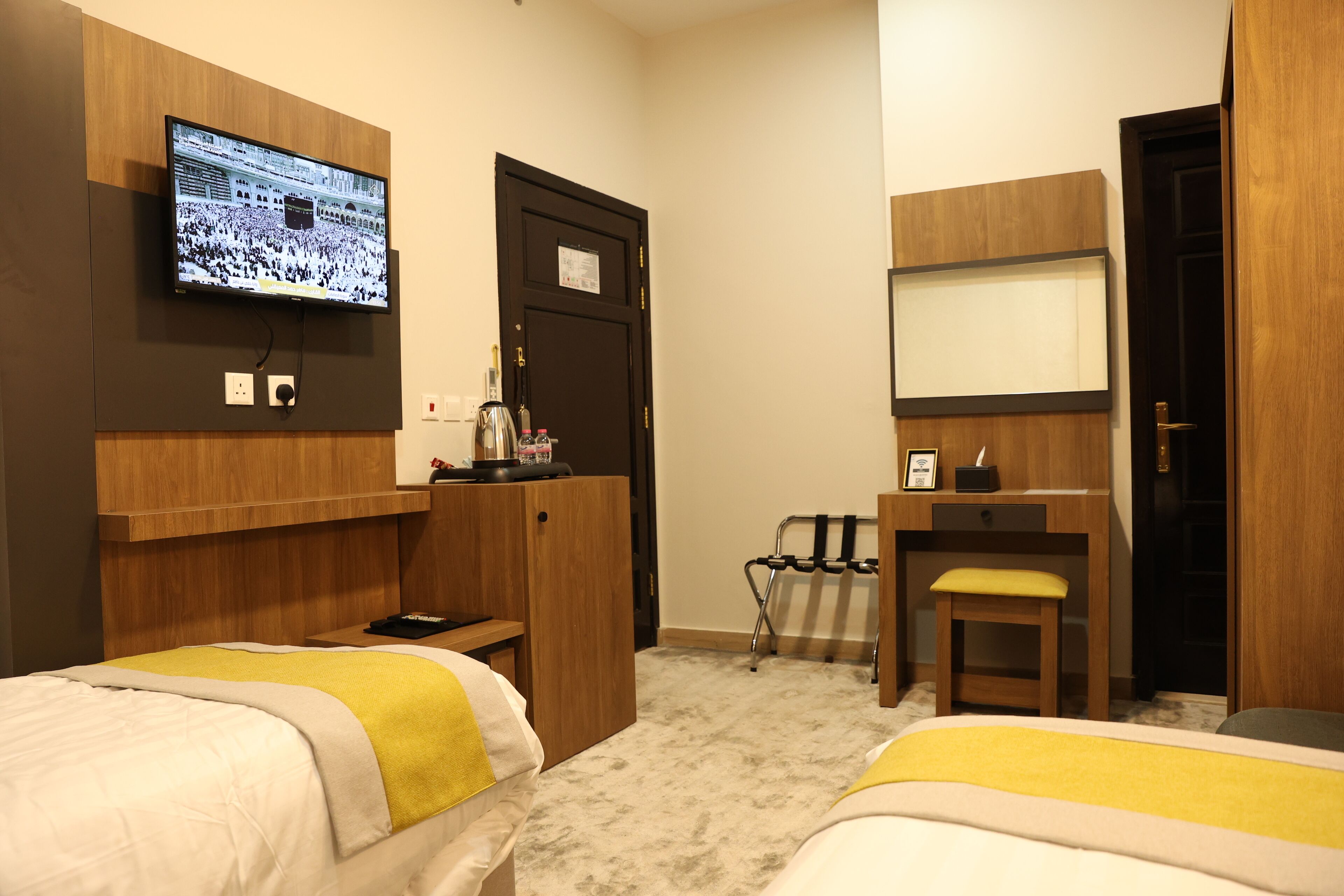 Habitación de hotel con dos camas, un escritorio, una silla, un televisor montado en la pared y una puerta.