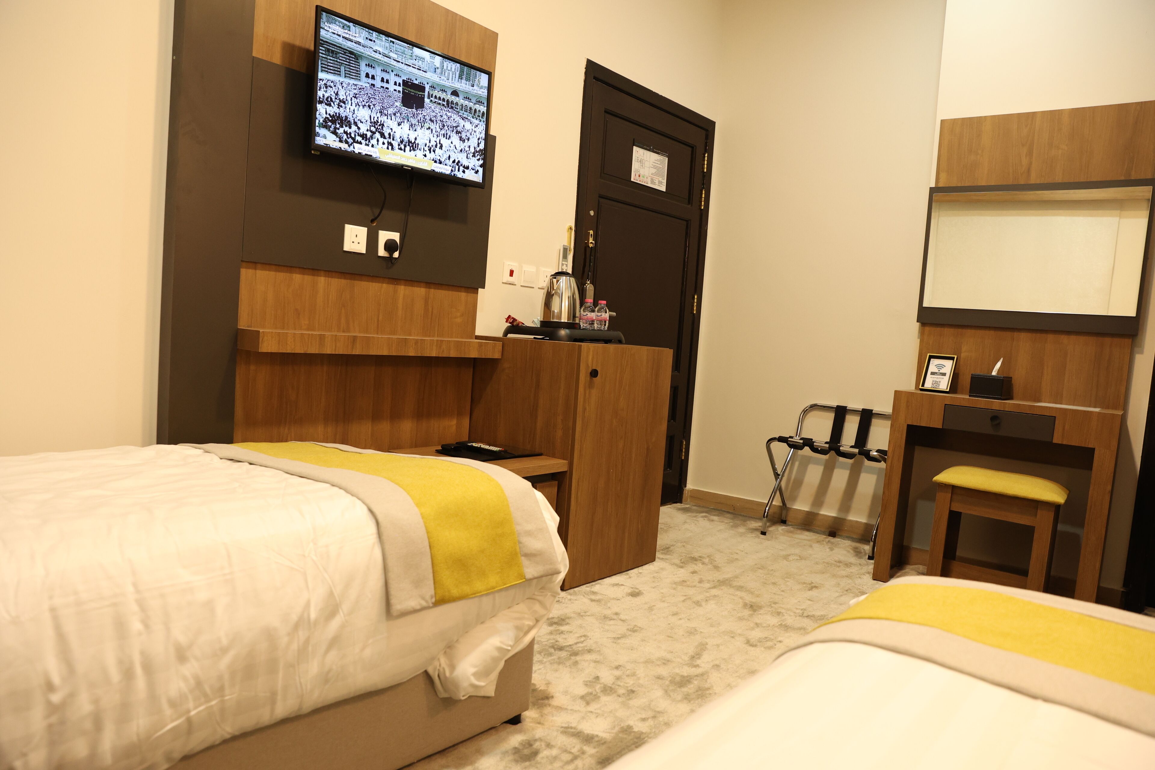 A hotel room with two beds, a desk, a chair, a television, and a door.