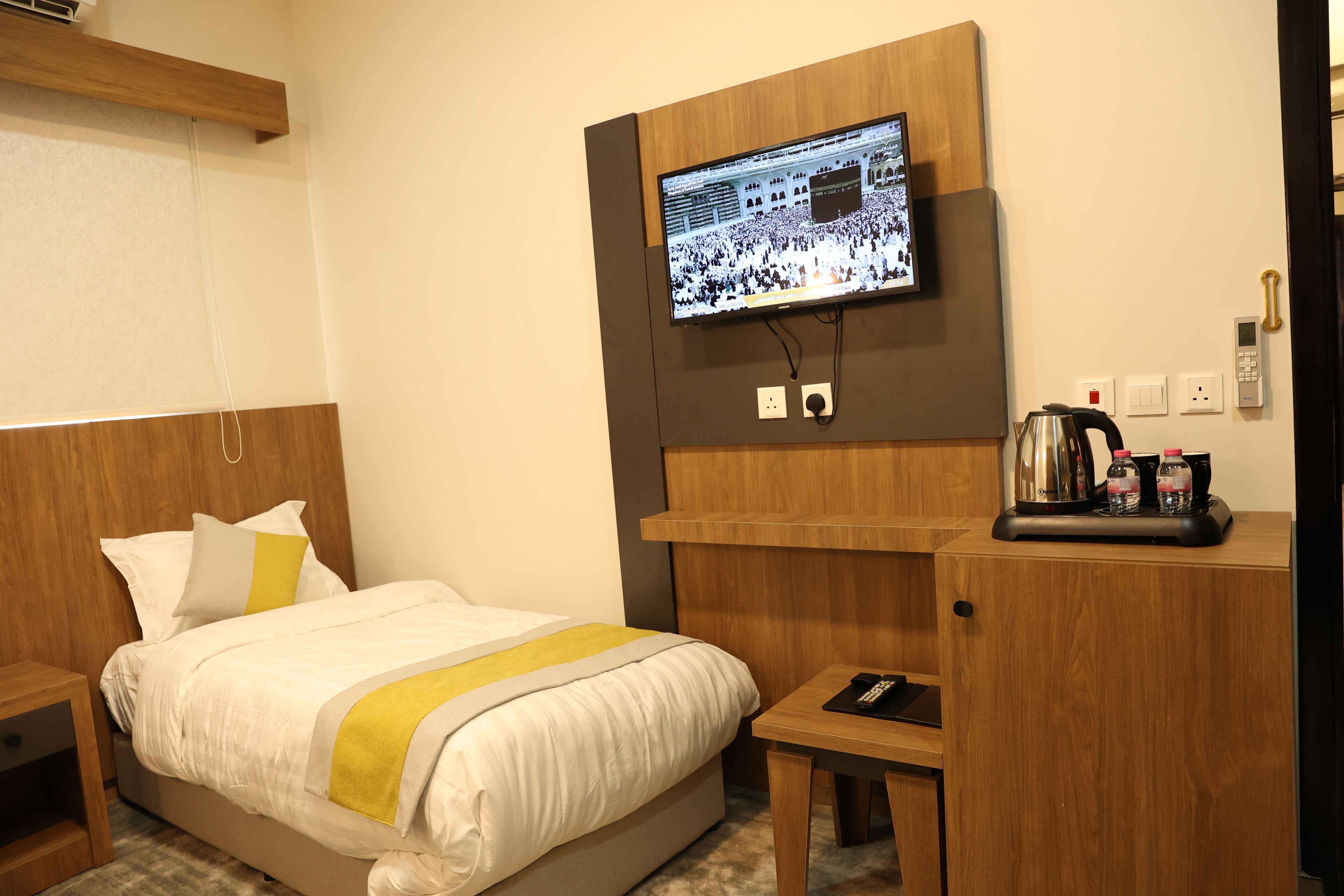 A hotel room with a bed, a desk, a television mounted on the wall, and a coffee maker on the desk.