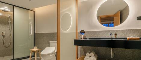 A modern bathroom with a glass-enclosed shower, a wooden stool, a toilet, a black vanity with a mirror, and a towel rack.
