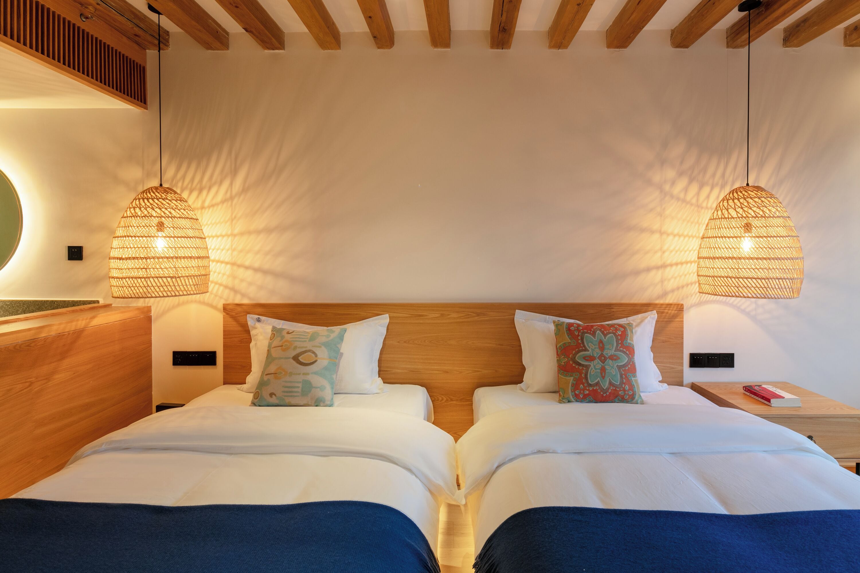 A double room with two beds, wooden headboards, and hanging wicker lamps.