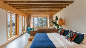 Een moderne slaapkamer met een groot bed, houten balken in het plafond, grote ramen en uitzicht op een traditioneel gebouw.