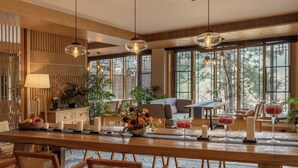 Een ruime eetruimte met een lange houten tafel, rieten stoelen en verschillende planten en kaarsen.