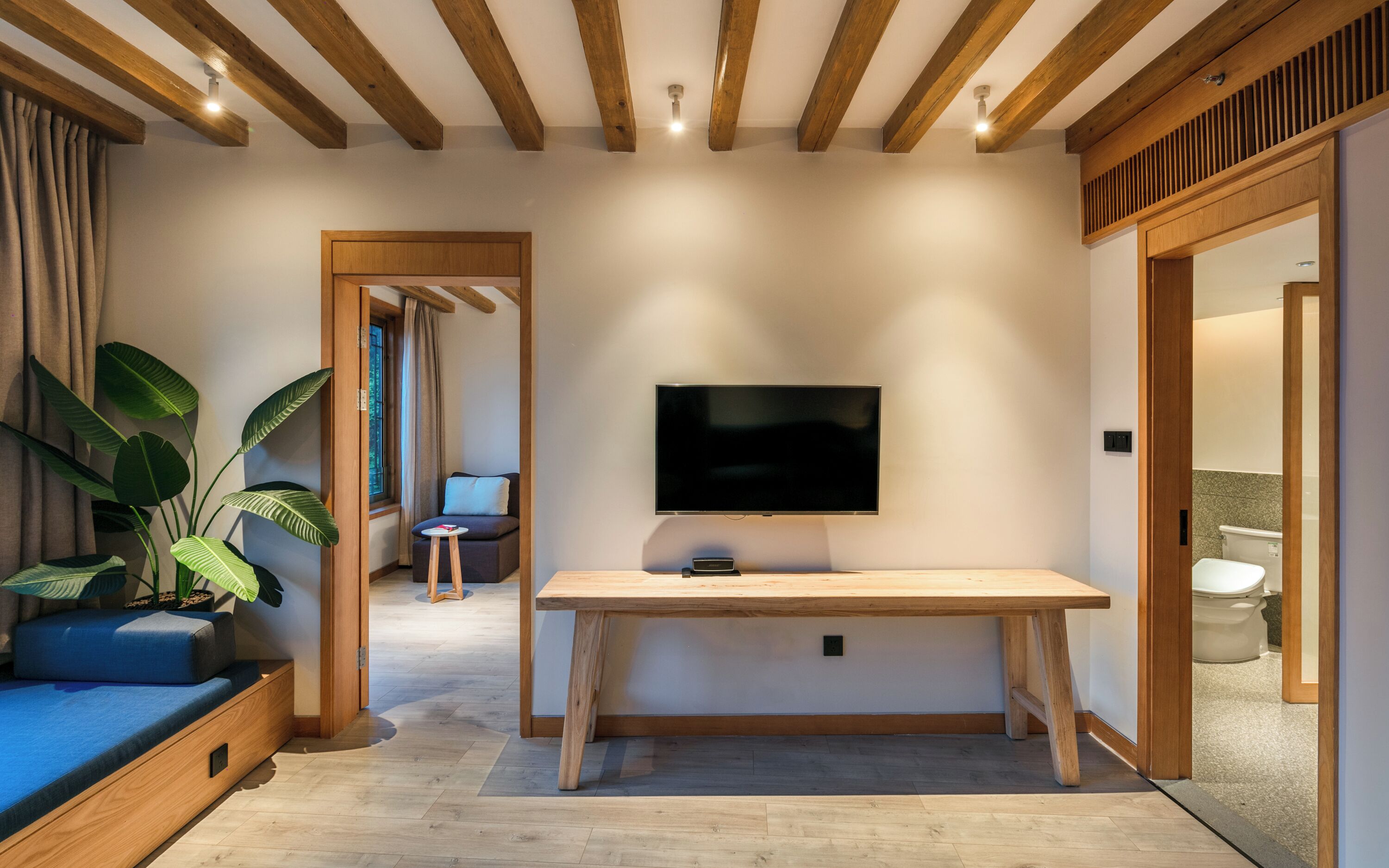 A modern living room with a wooden ceiling, a flat-screen TV mounted on the wall, a wooden dining table, and a blue sofa.