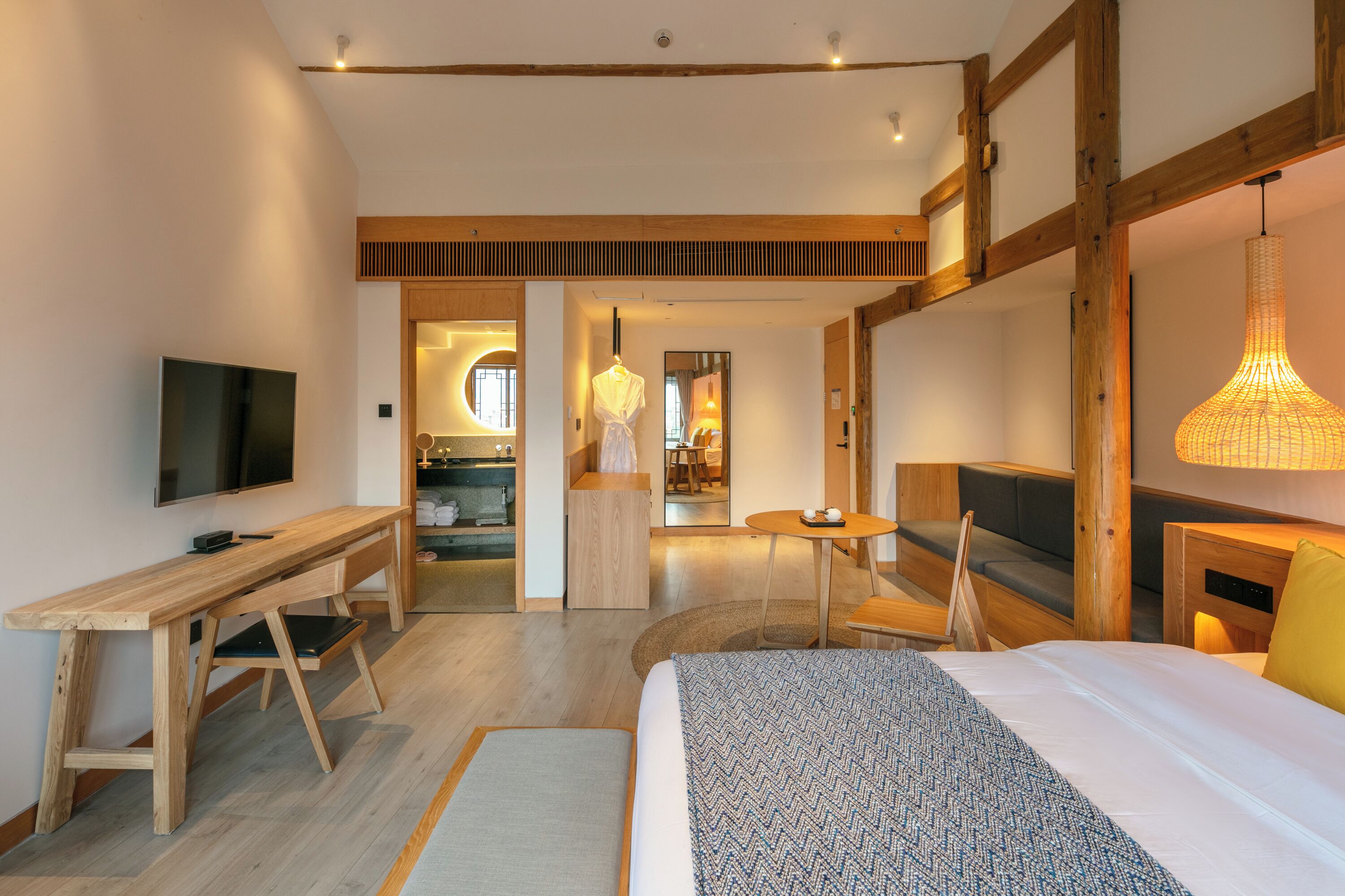 A modern hotel room with a wooden desk, a bed, a TV, and a dining area.